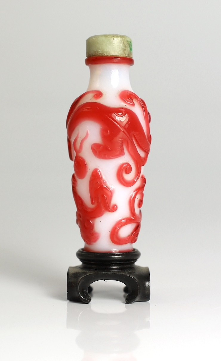 A Chinese red overlay on white glass ‘chilong’ snuff bottle, 1780-1850, 6.5cm high, wood stand